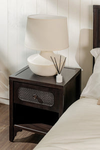 Dark wooden nightstand with a lamp and decorative items next to a bed.