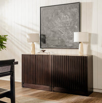 Wooden sideboard with two lamps and a painting in a room with wooden flooring.