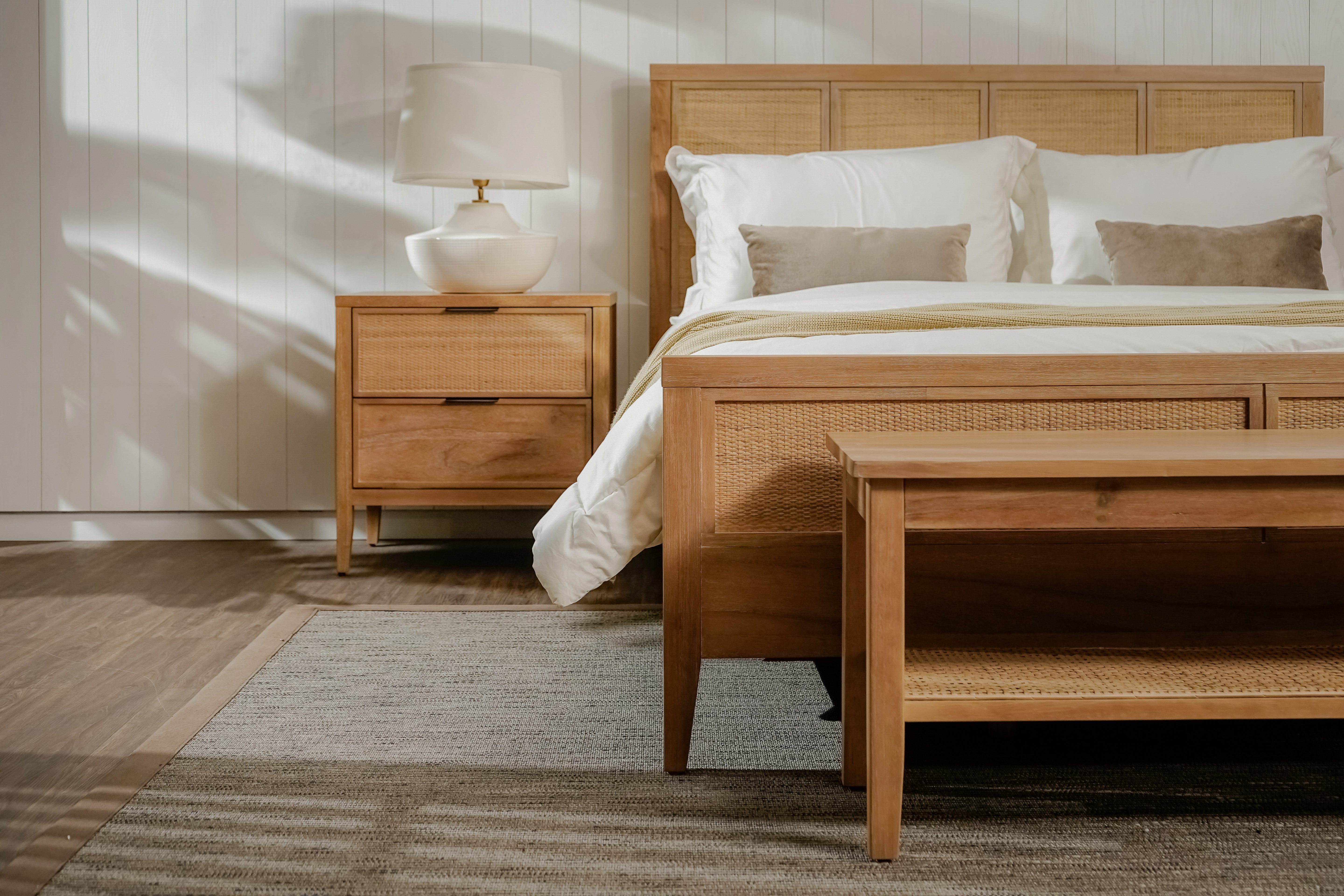 Wooden bedroom furniture set with bed, nightstand, and side table in a room with sunlight filtering through.