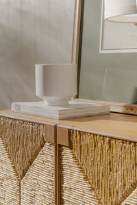Decorative cabinet with wicker design and a white vase on top