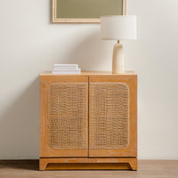 Wooden cabinet with wicker doors and a lamp on top against a plain wall.