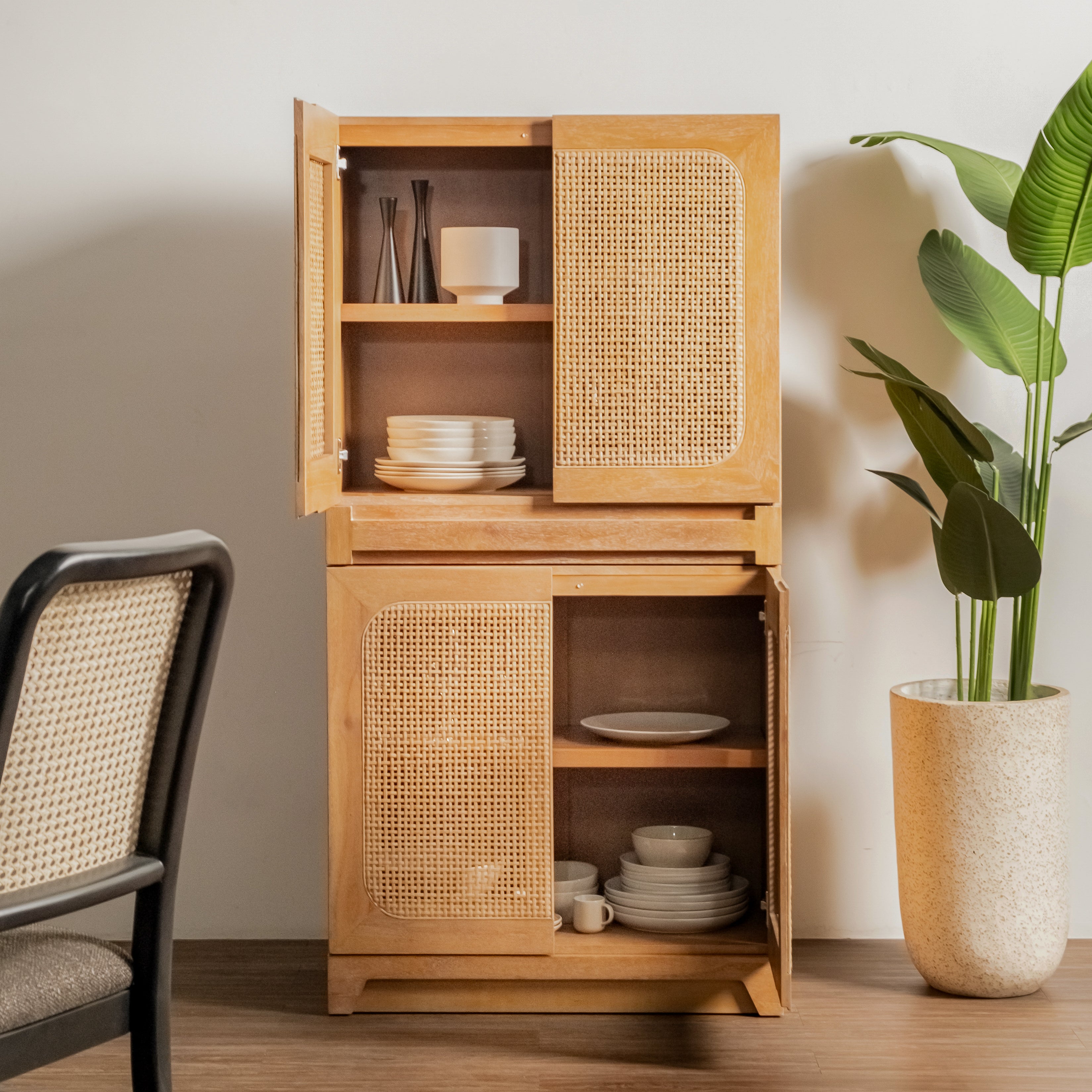 Wooden cabinet with wicker doors containing kitchenware, next to a chair and plant.