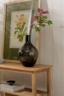 Decorative setup with a framed botanical print, black vase, and flowers on a wooden shelf.