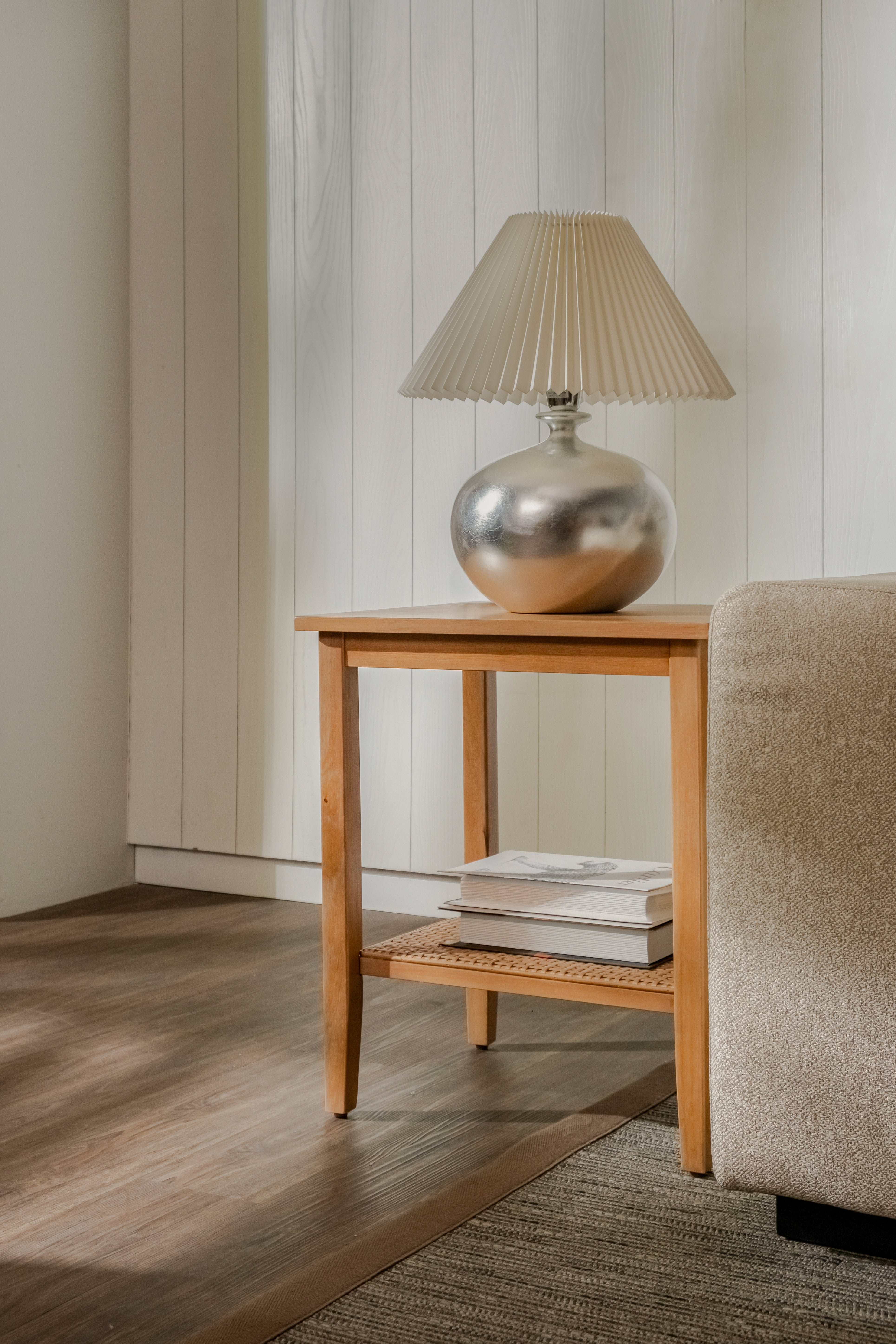 Wooden side table with a silver lamp and books against a neutral wall.