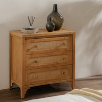 Wooden chest of drawers with wicker-style handles and decorative vases on top.