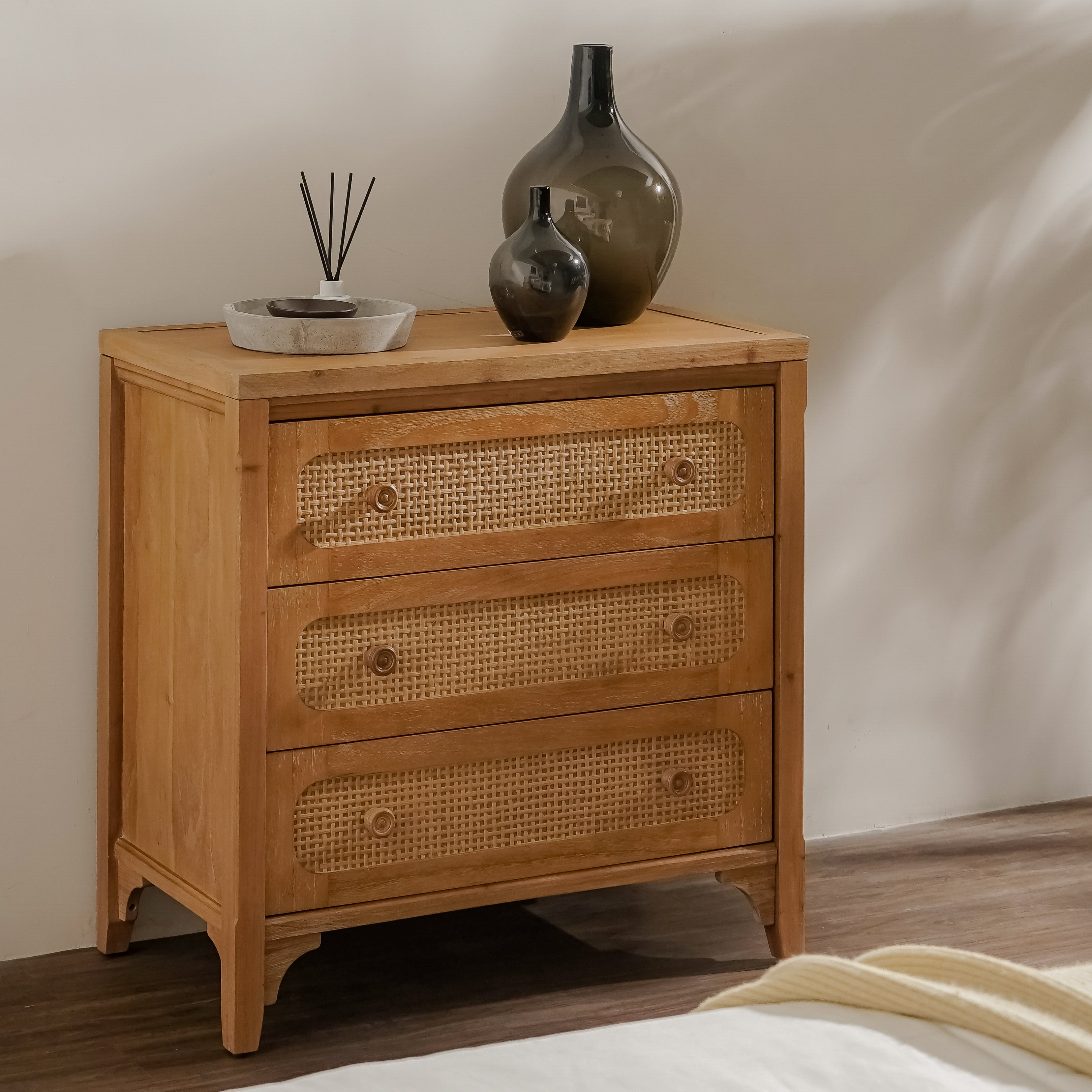 Wooden chest of drawers with wicker-style handles and decorative vases on top.
