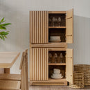 Wooden cabinet with open doors displaying glasses and plates in a room with a table and plants.