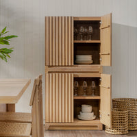Wooden cabinet with open doors displaying glasses and plates in a room with a table and plants.