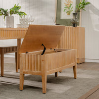 Wooden storage bench with open lid in a room with a table and plants.
